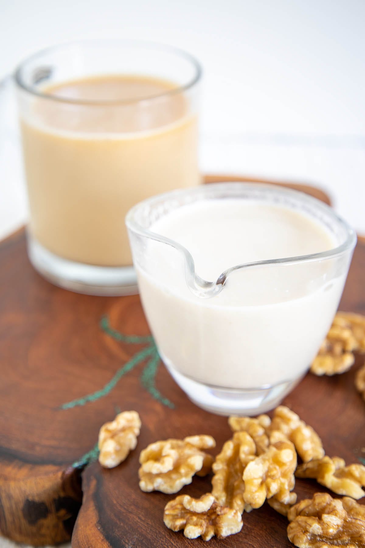 Homemade Walnut Milk in a pitcher with a mug of tea in the background.