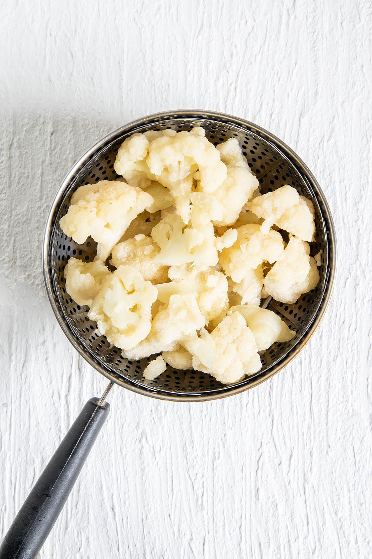 Cauliflower in a steamer basket above a saucepan.