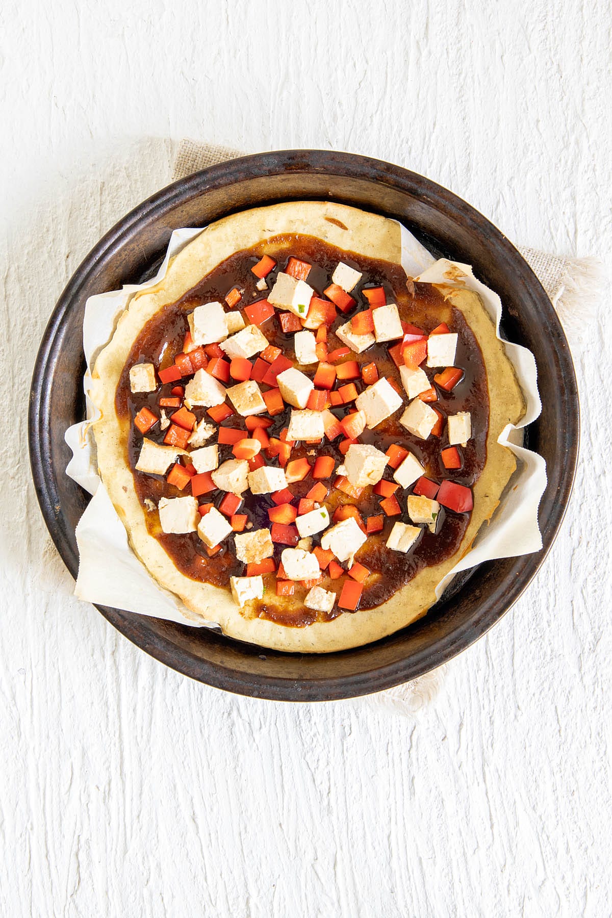 Pizza crust with red pepper, tofu, and hoisin sauce before baking.
