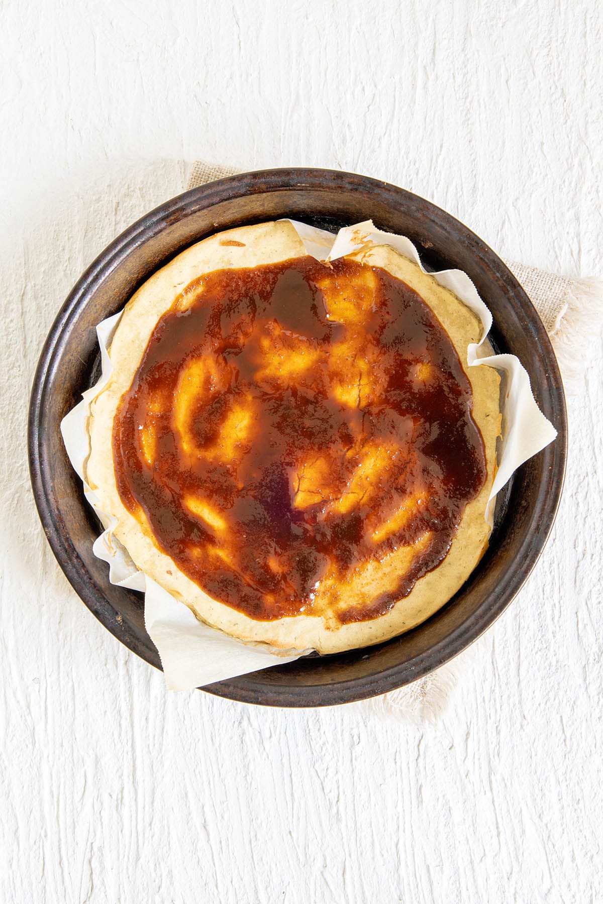 Pizza crust in a pan with hoisin sauce on top.
