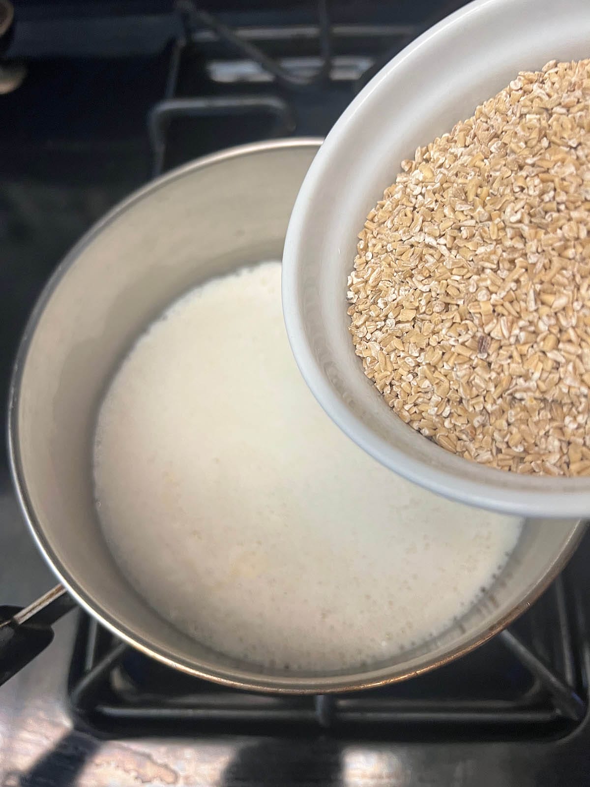 Saucepan with almond milk that is simmering. Steel cut oats being poured into the pan.