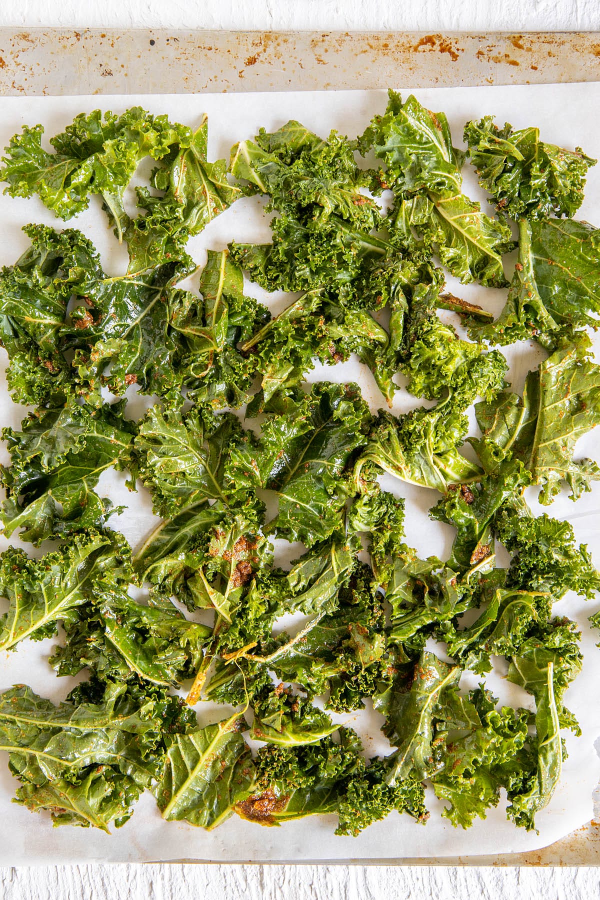 Kale pieces with seasoning on a parchment paper lined baking sheet.