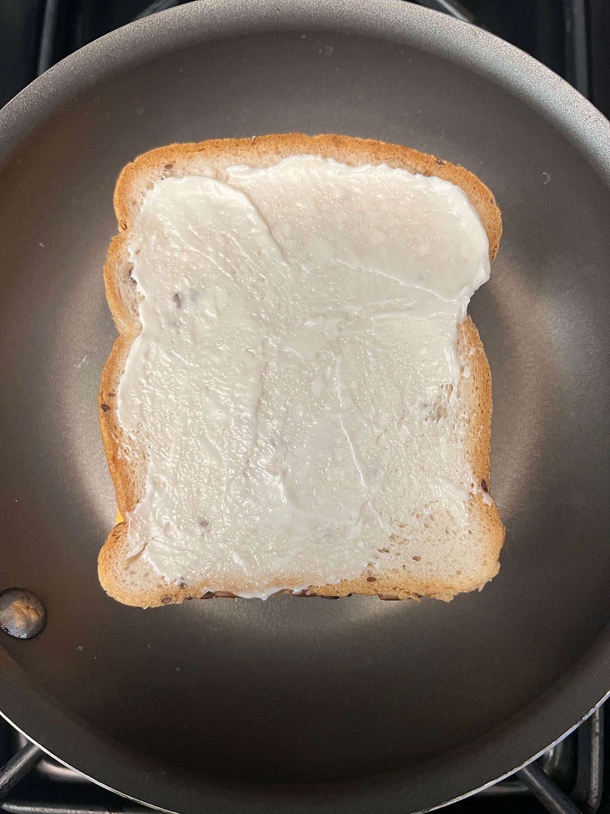 Refried bean sandwich in a skillet with vegan mayo on the outside of bread.