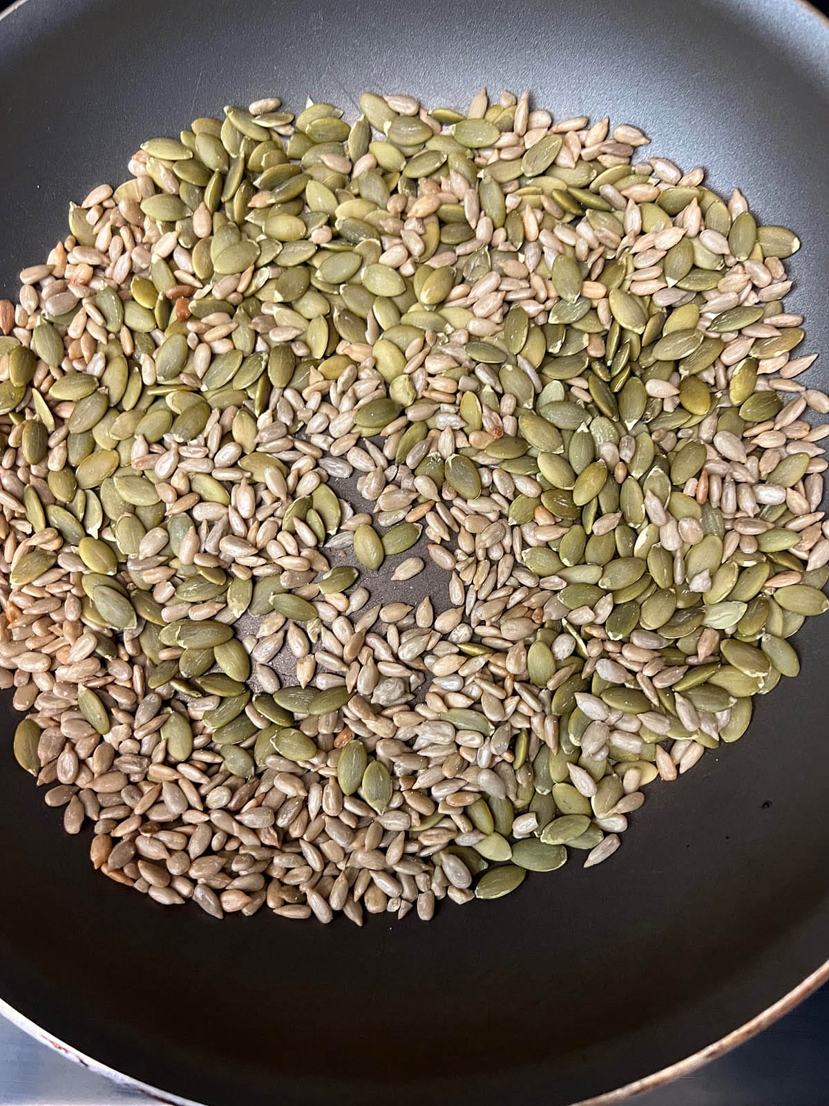 Pumpkin seeds and sunflowers seeds in a skillet.