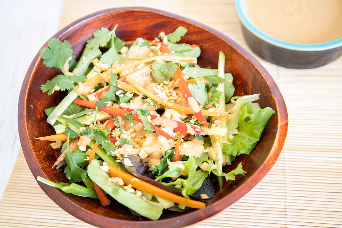 Thai Salad in a wood bowl with peanut sauce in the background.