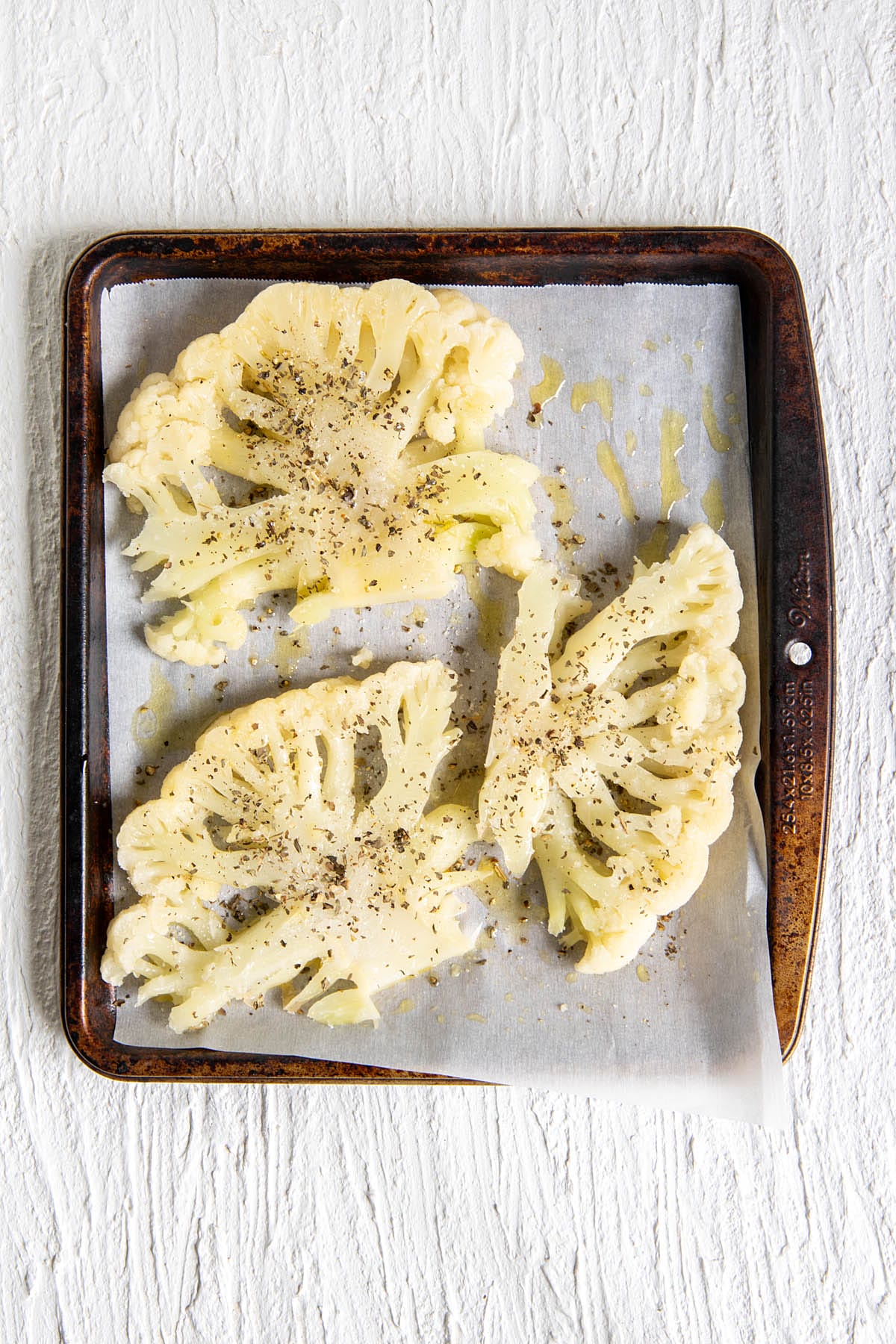 Cauliflower steaks on a parchment paper lined baking sheet.