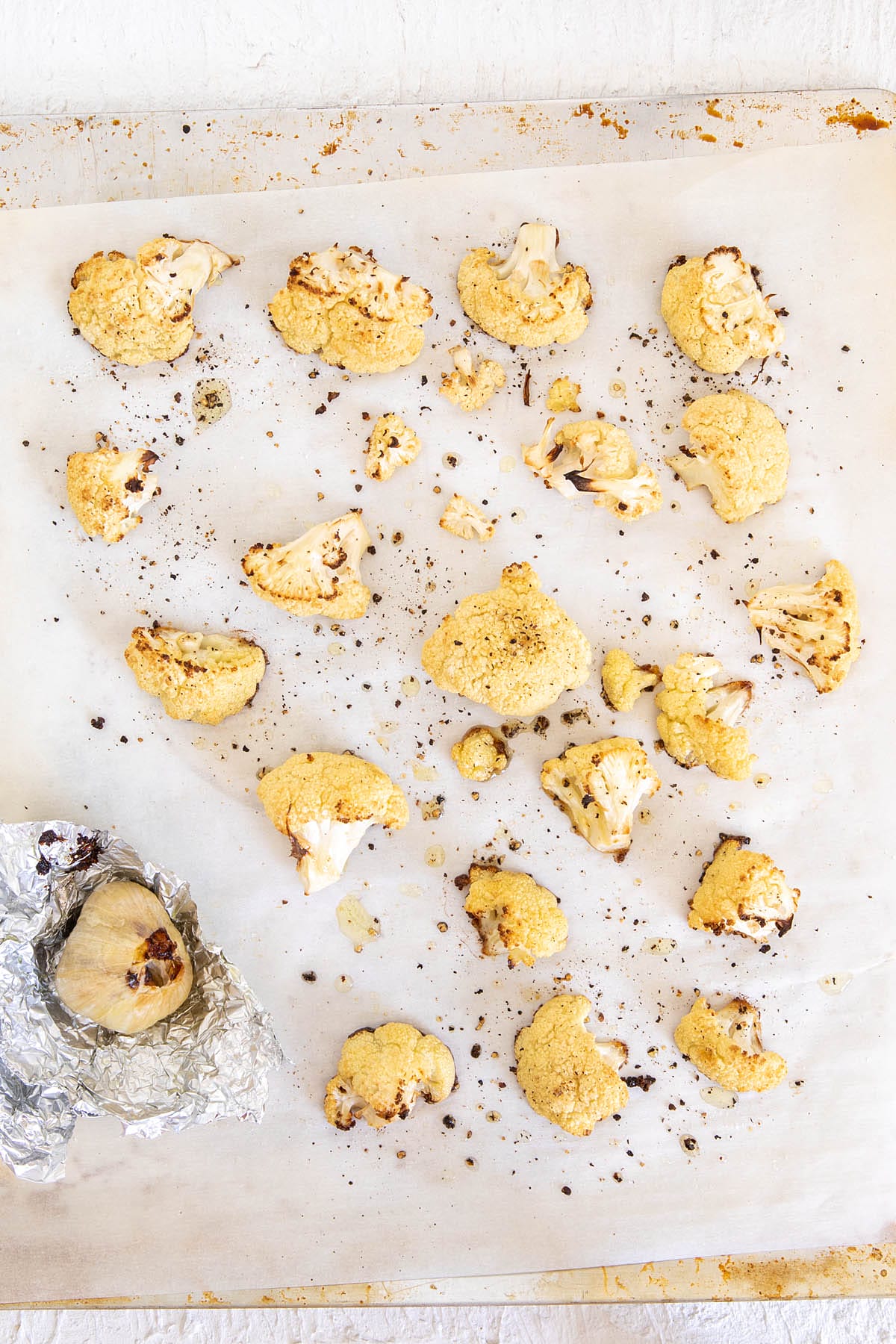 Roasted cauliflower and garlic on a parchment paper lined baking sheet.