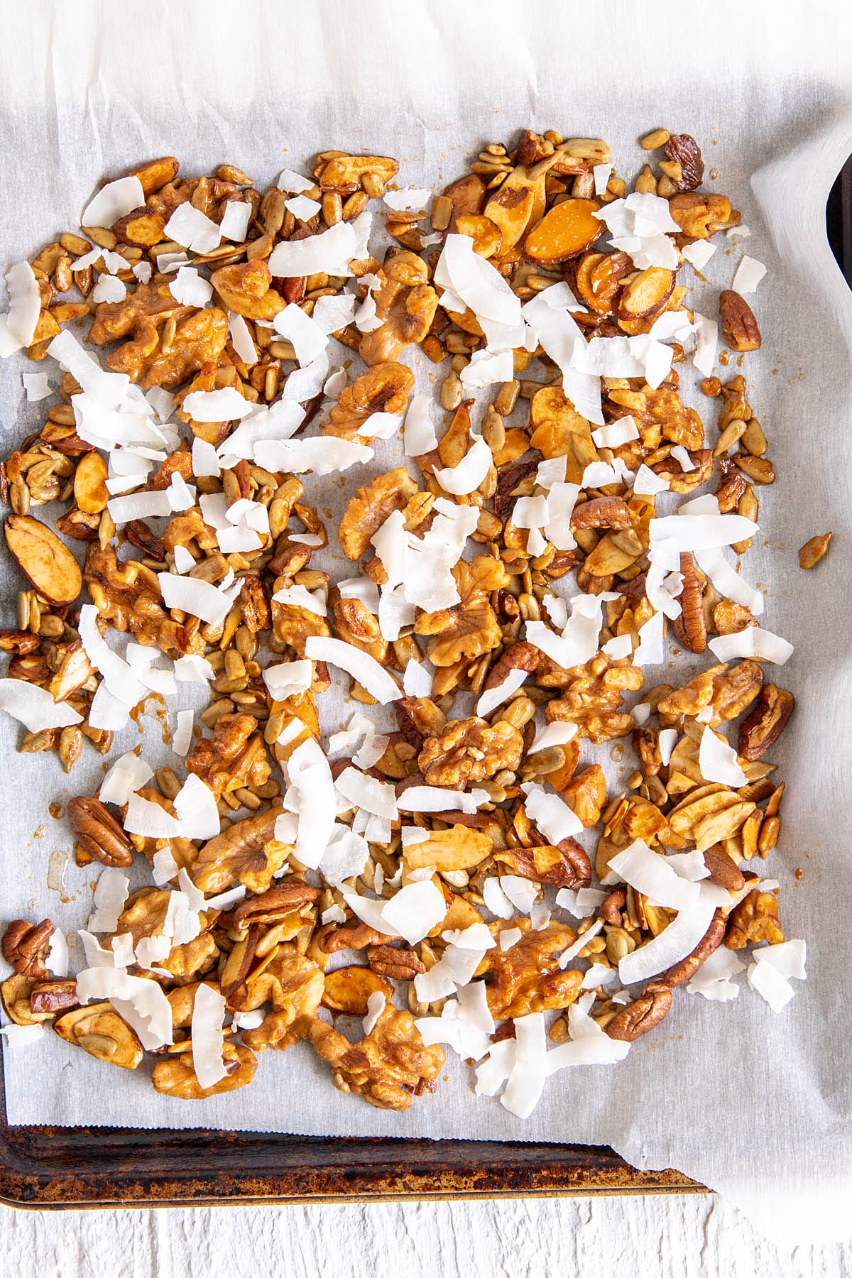 Nut mixture with the addition of coconut chips on a parchment paper lined baking sheet.
