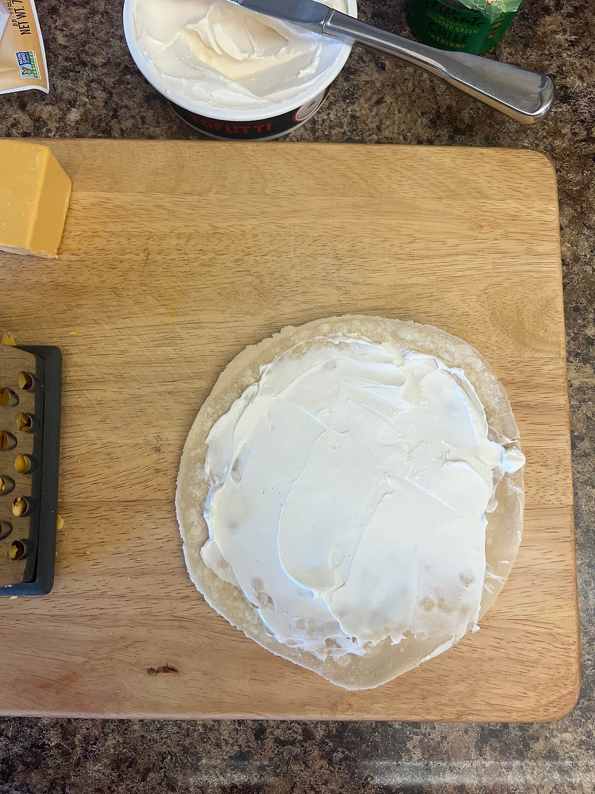 Tortilla with cream cheese on a cutting board.