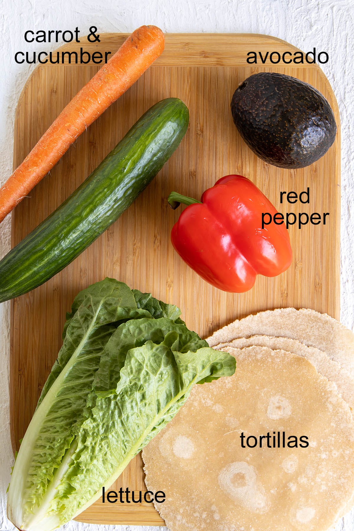 Vegan veggie wrap ingredients on a cutting board with labels.