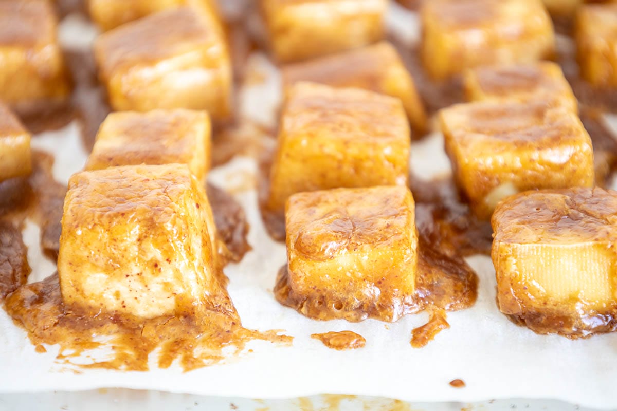 Baked tofu with  peanut sauce on a parchment paper lined baking sheet.