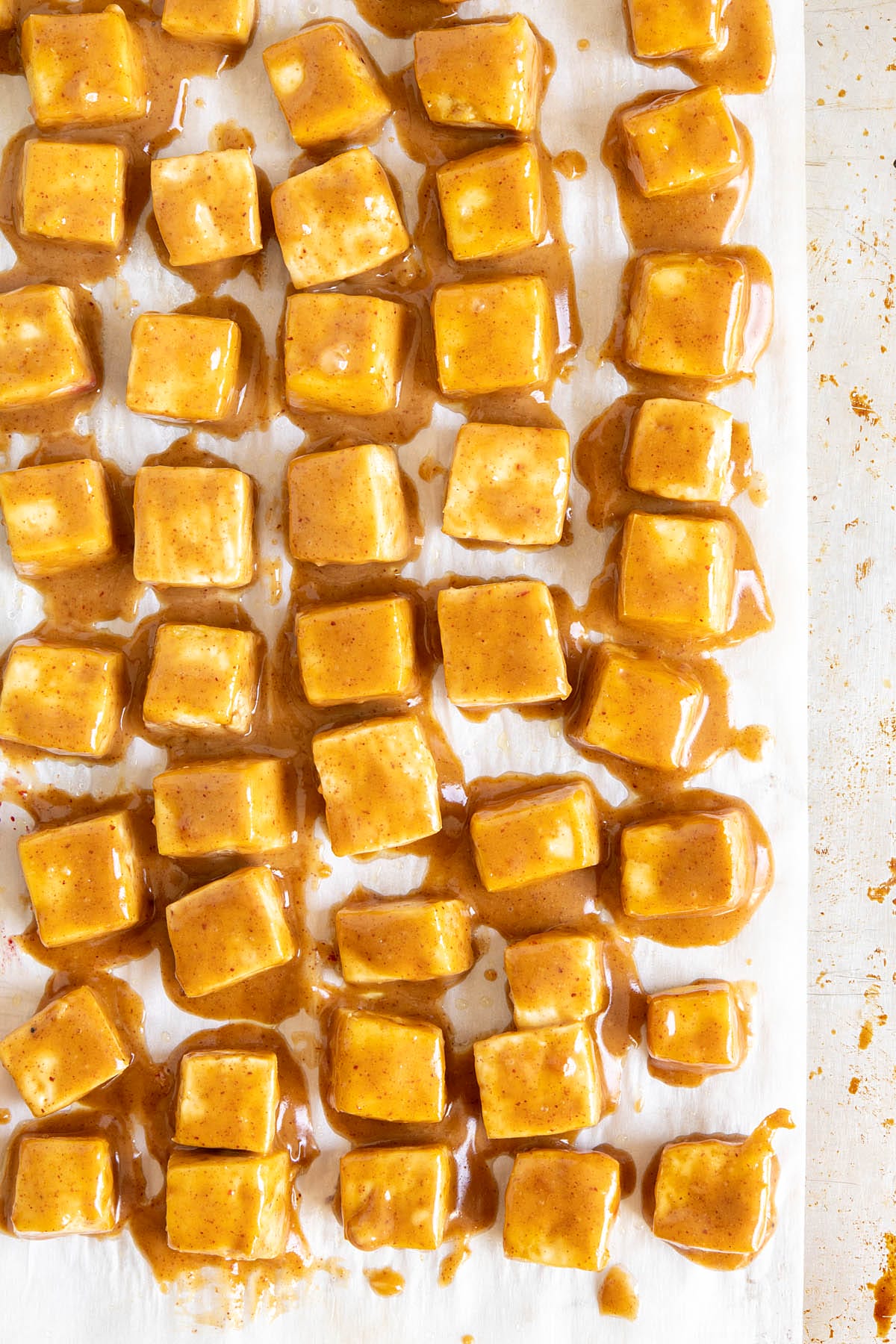Cubed tofu with peanut sauce on a parchment paper lined baking sheet.