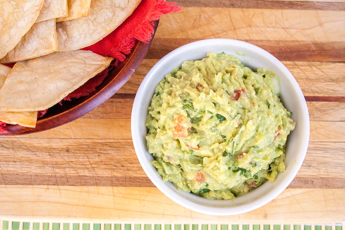 Guacamole in a small bowl with baked tortilla chips next to them.