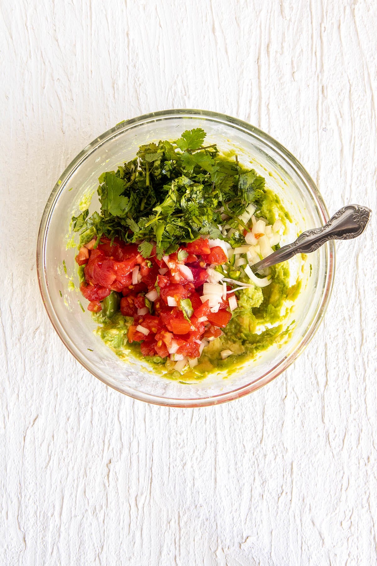 Tomatoes, onions, and cilantro added to the bowl with mashed avocados.