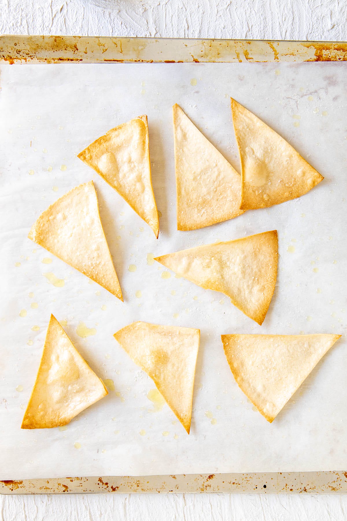 Baked tortilla chips on a parchment paper lined baking sheet.