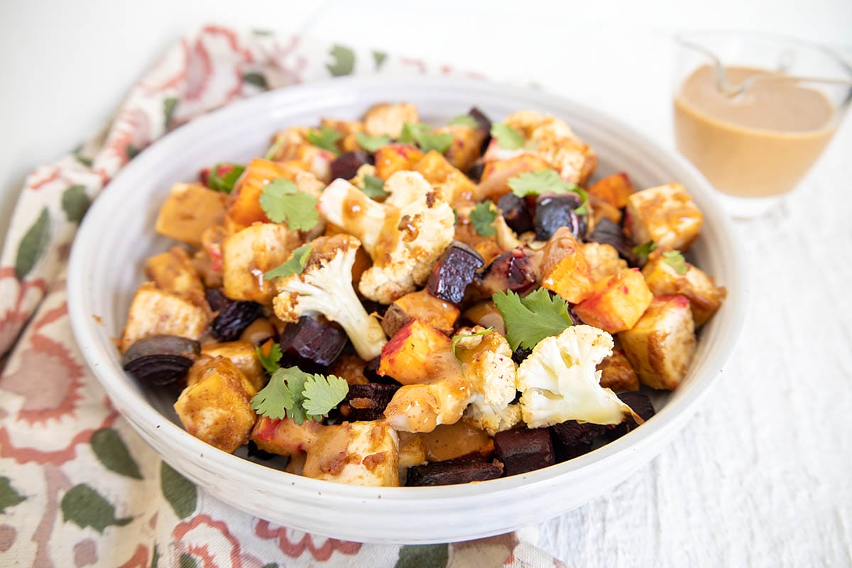 Tofu and veggies in a bowl with peanut sauce in background.
