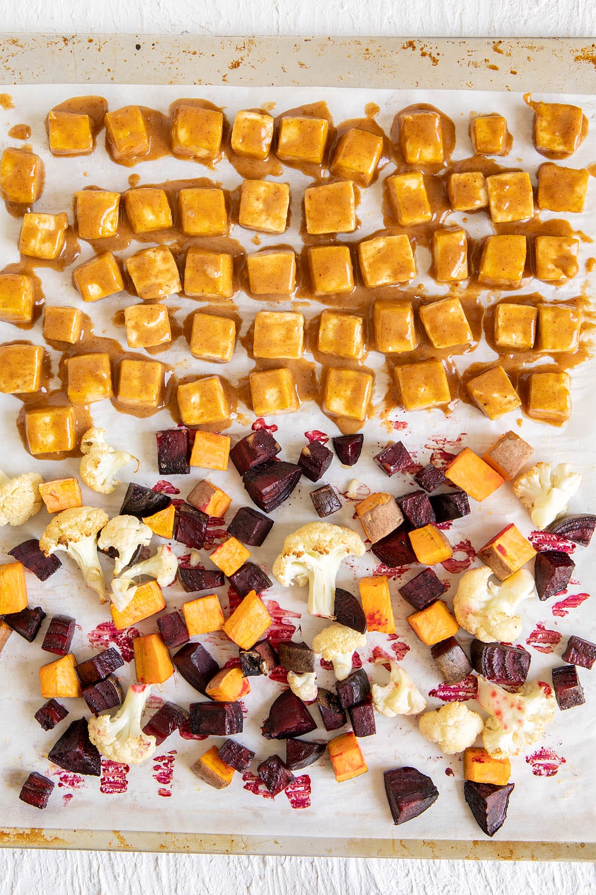 Cubed tofu with peanut sauce and vegetables on a parchment paper lined baking sheet.