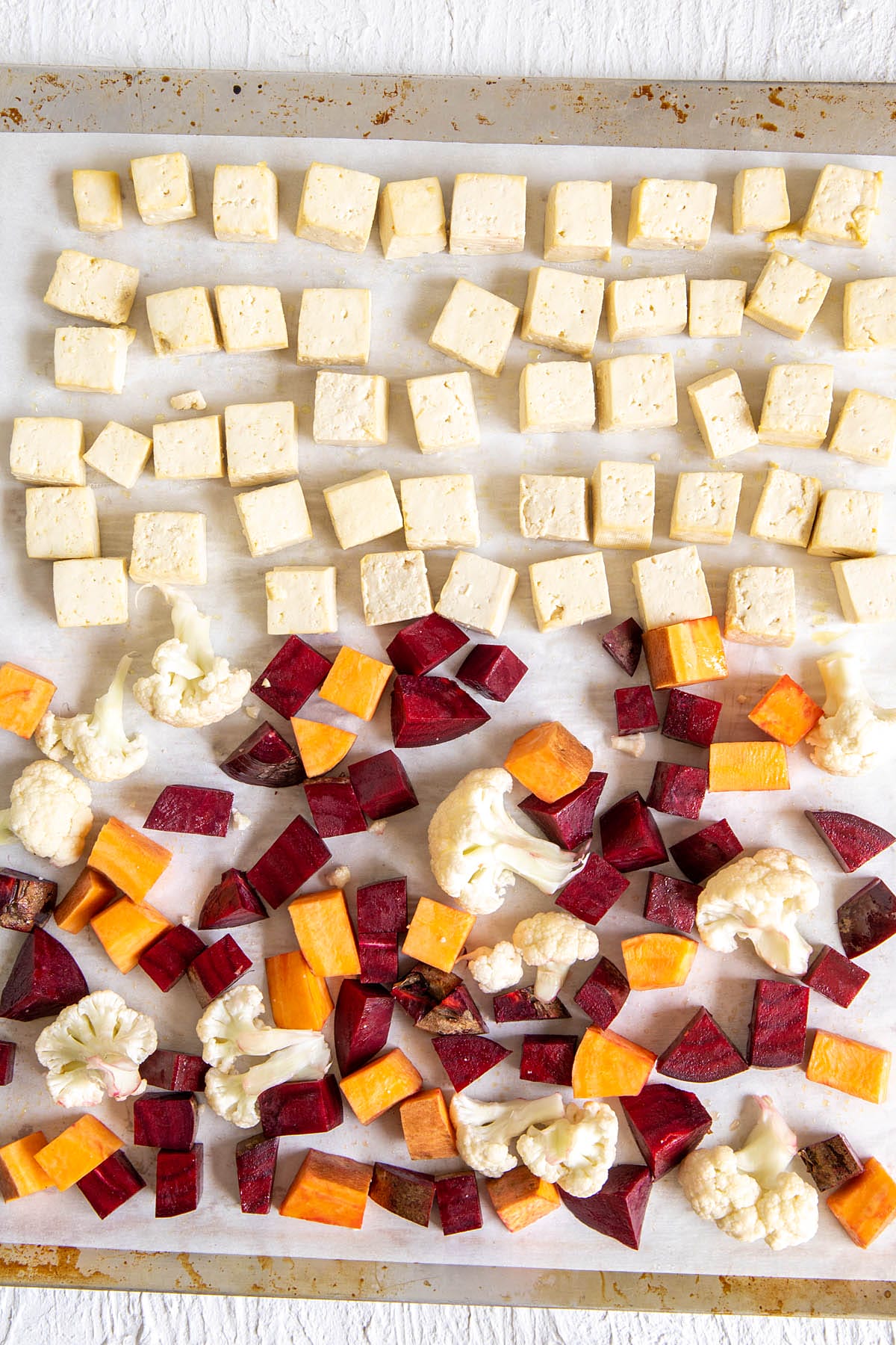 Cubed tofu and vegetables on a parchment paper lined baking sheet.