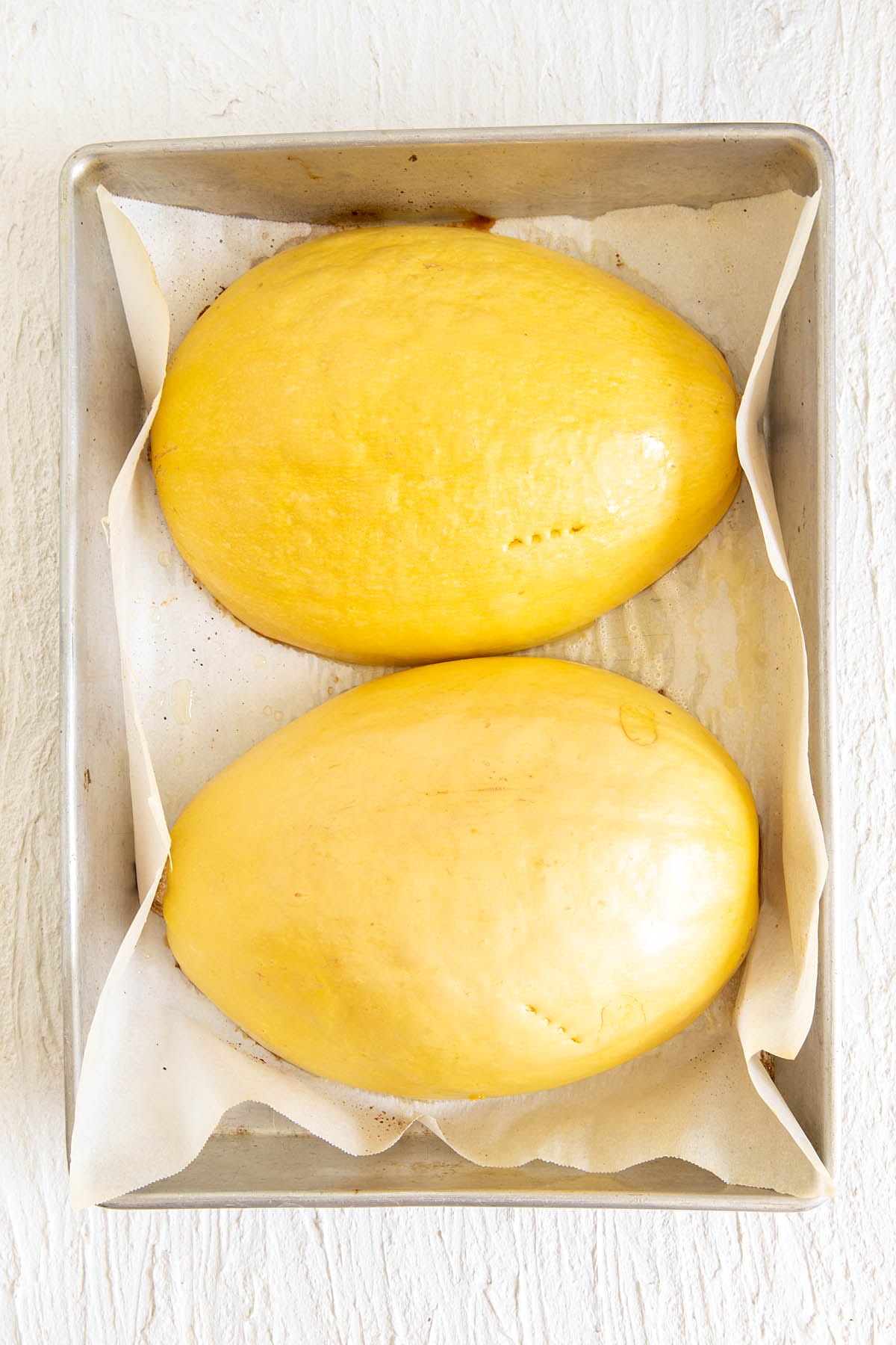 Roasted spaghetti squash cut in half on a parchment paper lined baking dish.
