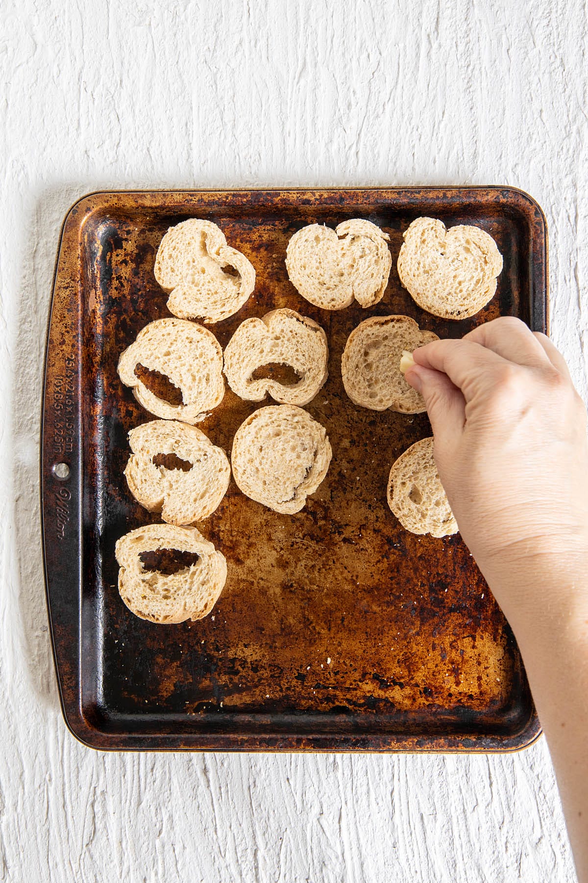 Garlic being rubbed on a sliced baguette on a baking sheet.
