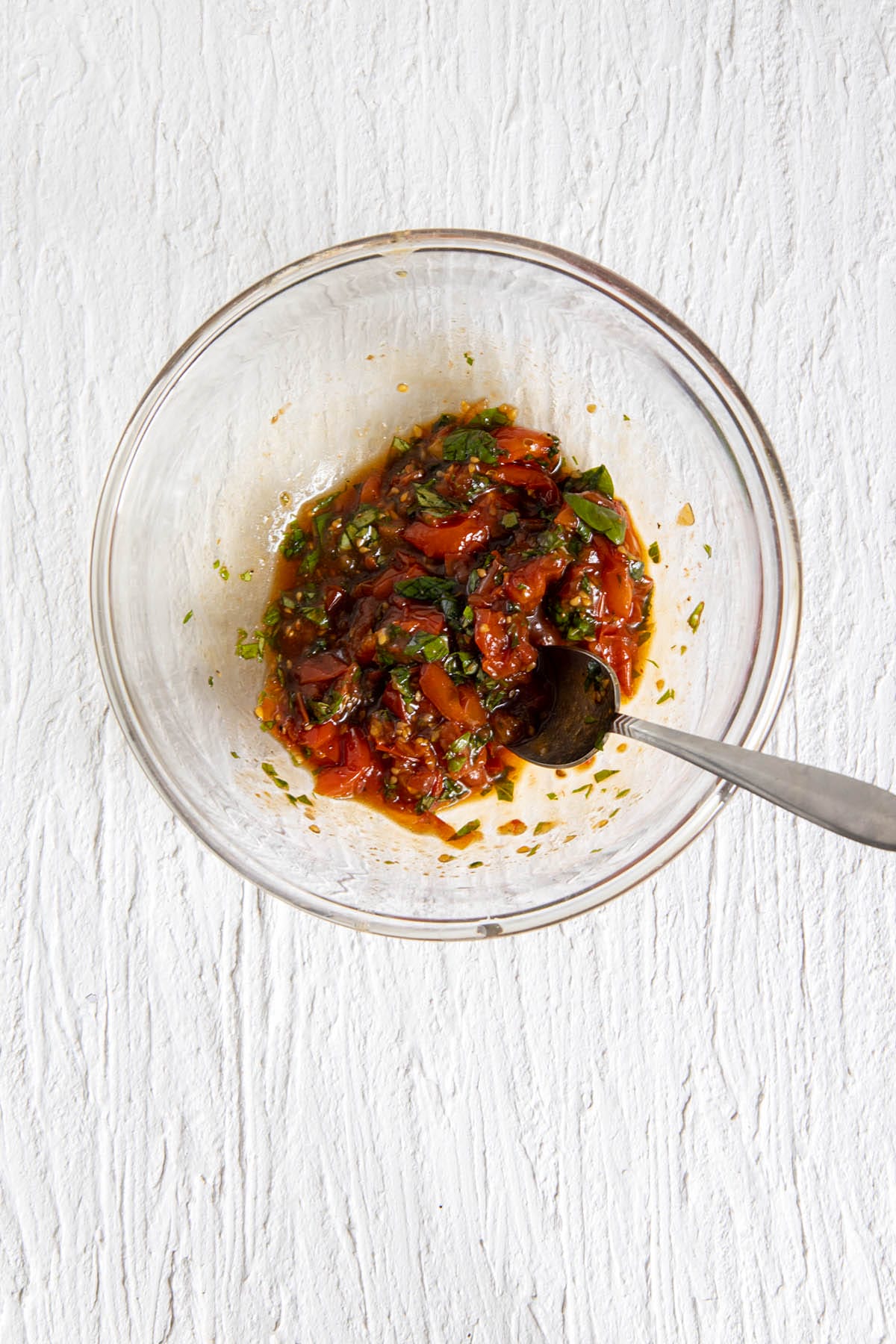Roasted tomato basil mixture in a mixing bowl with spoon.