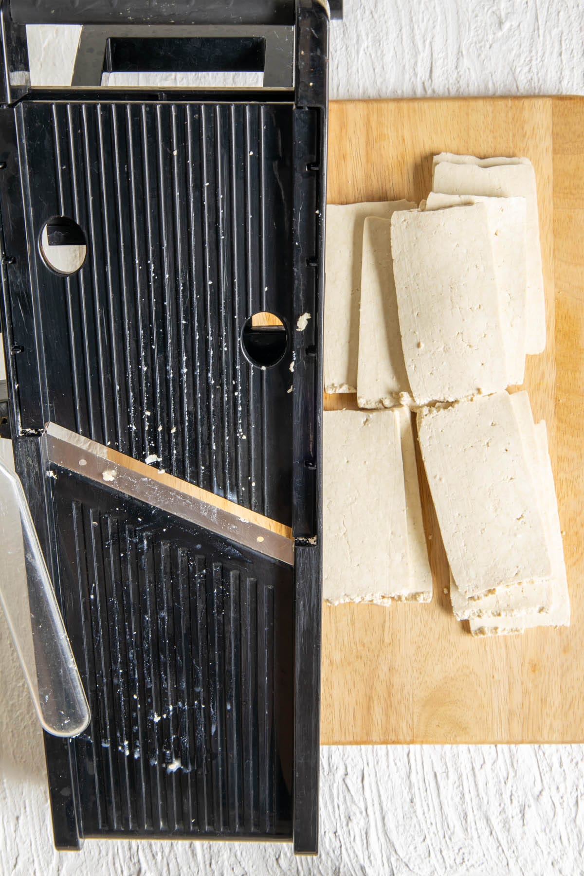 Sliced super firm tofu on a cutting board with mandoline.