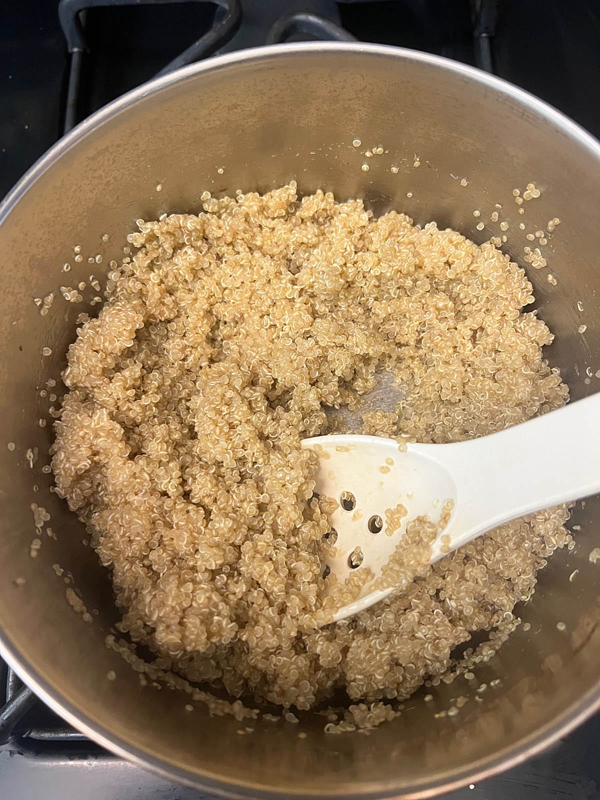 Cooked quinoa in a saucepan with spoon.