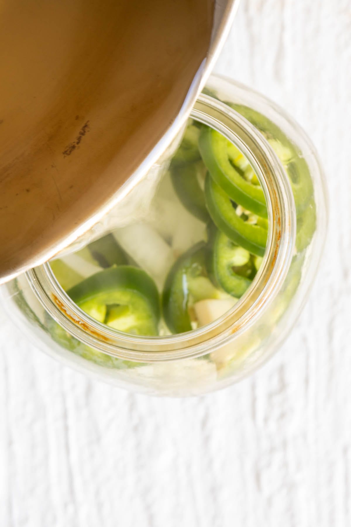 Vinegar mixture being poured into mason jar with peppers and onions.