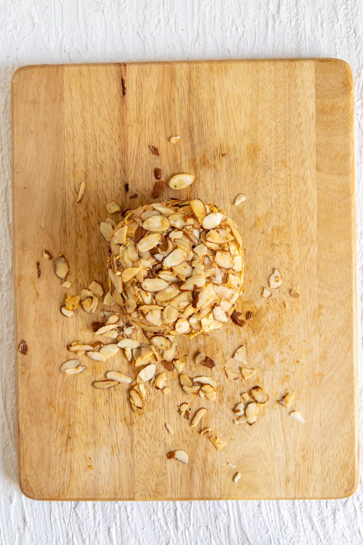 Vegan cheese ball rolled in sliced almonds on a cutting board.