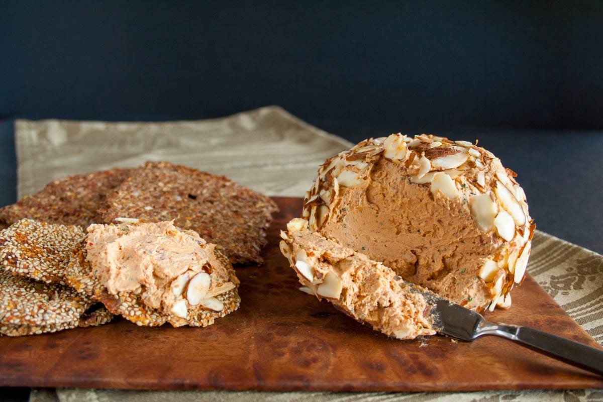Sun-Dried Tomato and Basil Vegan Cheese Ball on cutting board with crackers.