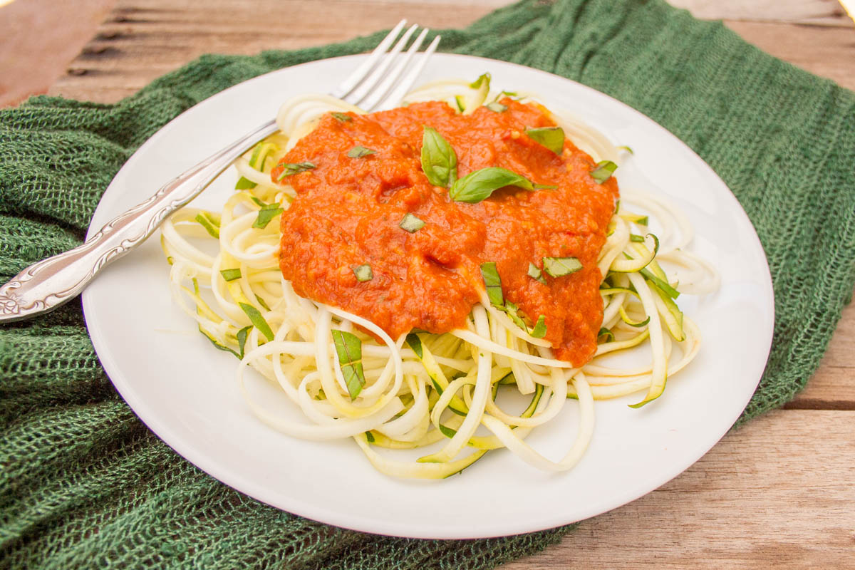 Zucchini noodles with roasted red pepper sauce on a plate with fork.