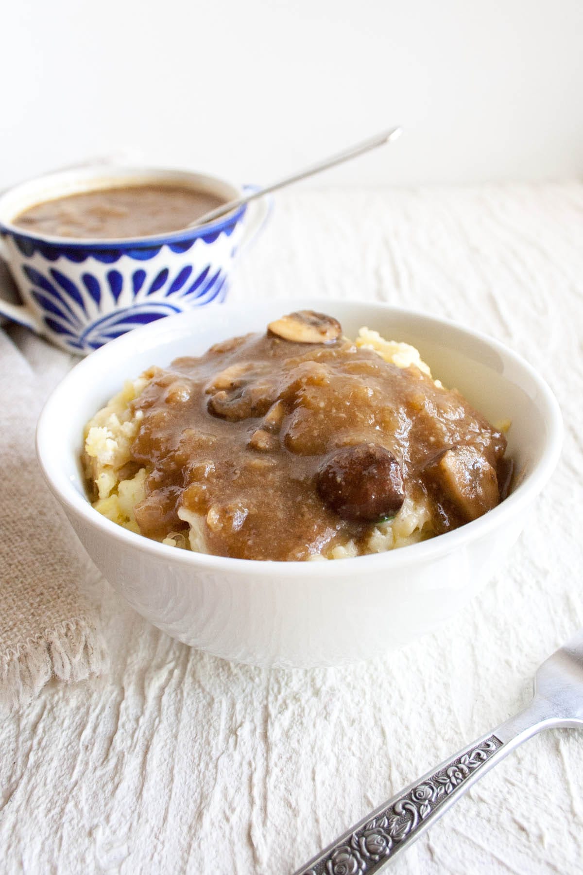 Vegan Caramelized Onion and Mushroom Gravy on potatoes in a bowl with gravy in the background.