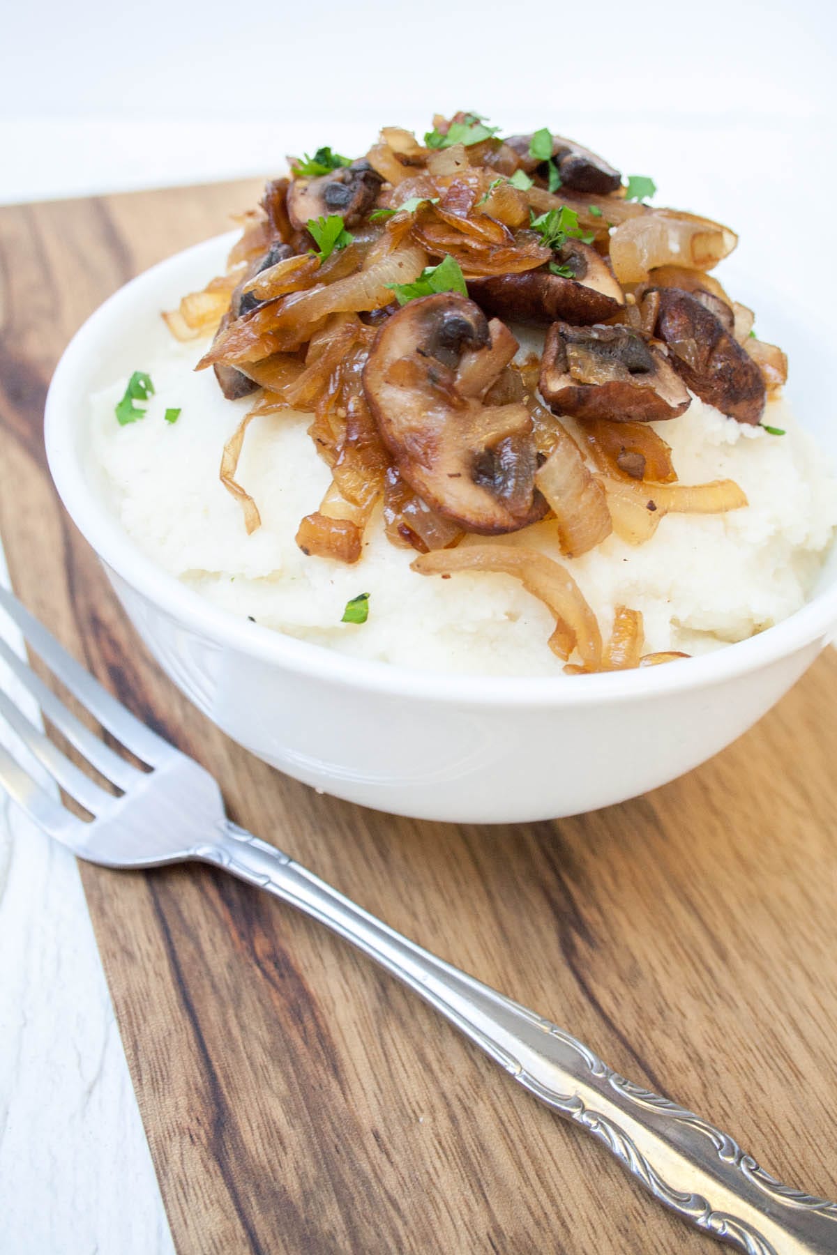 These Vegan Cauliflower Recipes showcase how versatile cauliflower is. From cauliflower rice to a smoothie, there's something for everyone! Vegan Mashed Cauliflower with Caramelized Onions and Mushrooms close up with fork on cutting board.
