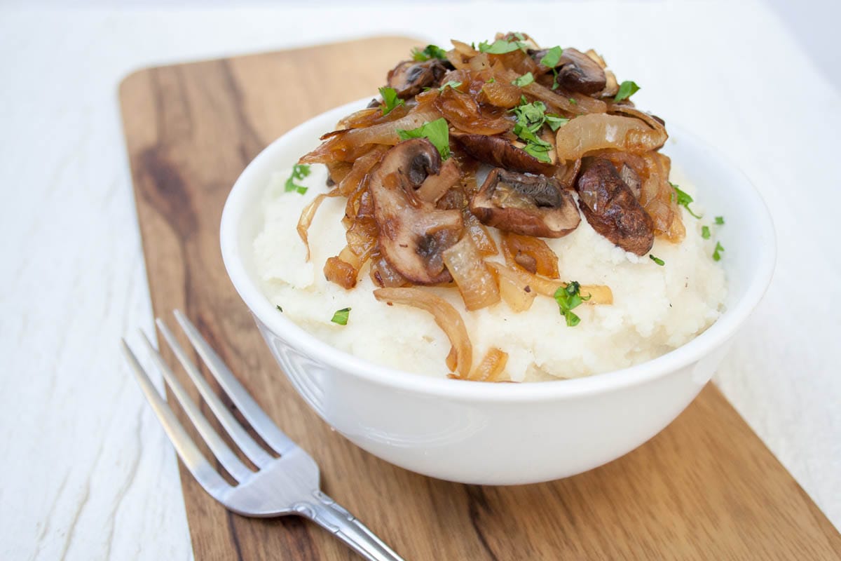 Vegan Mashed Cauliflower with Caramelized Onions and Mushrooms close up with fork on cutting board.