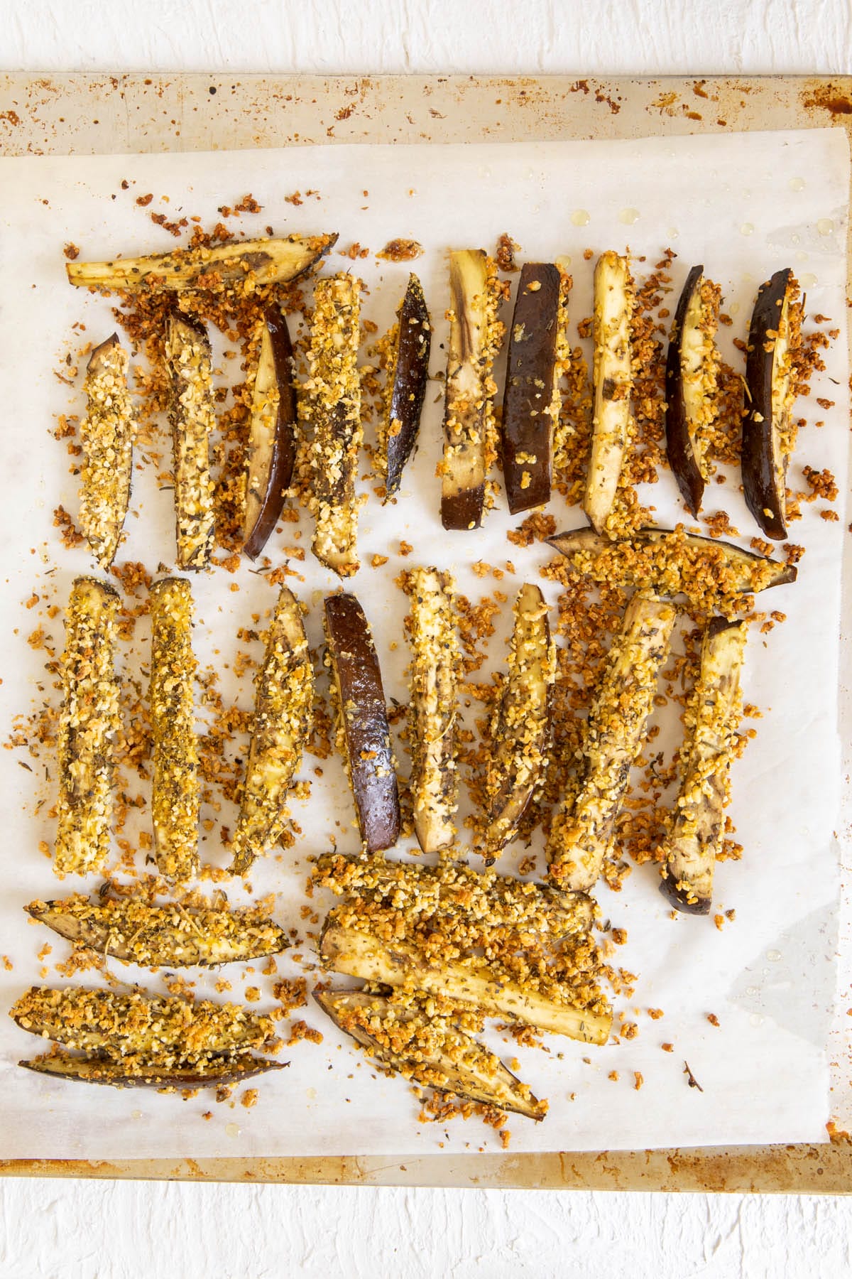 Baked eggplant fries on a parchment paper lined baking sheet.