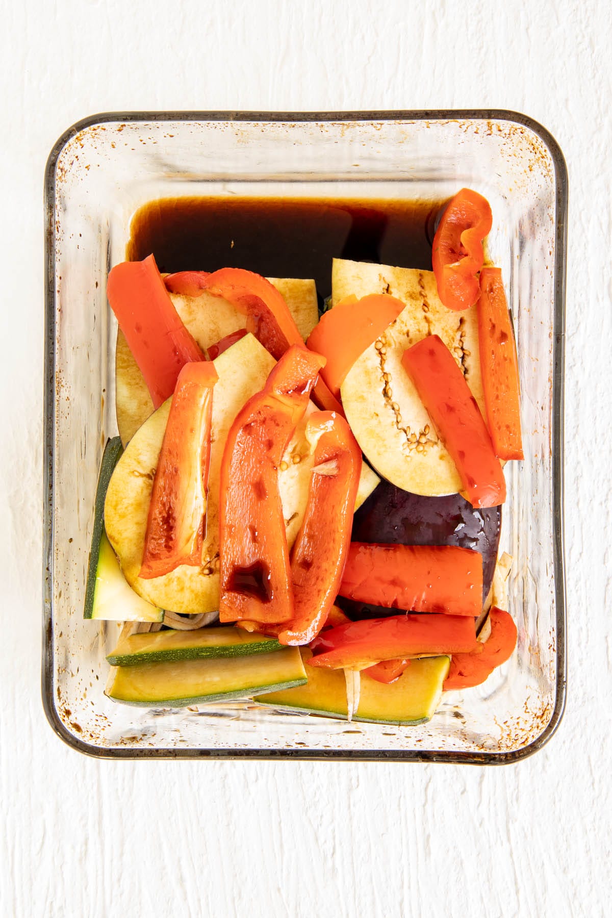 Sliced vegetables in a baking dish with balsamic vinegar.