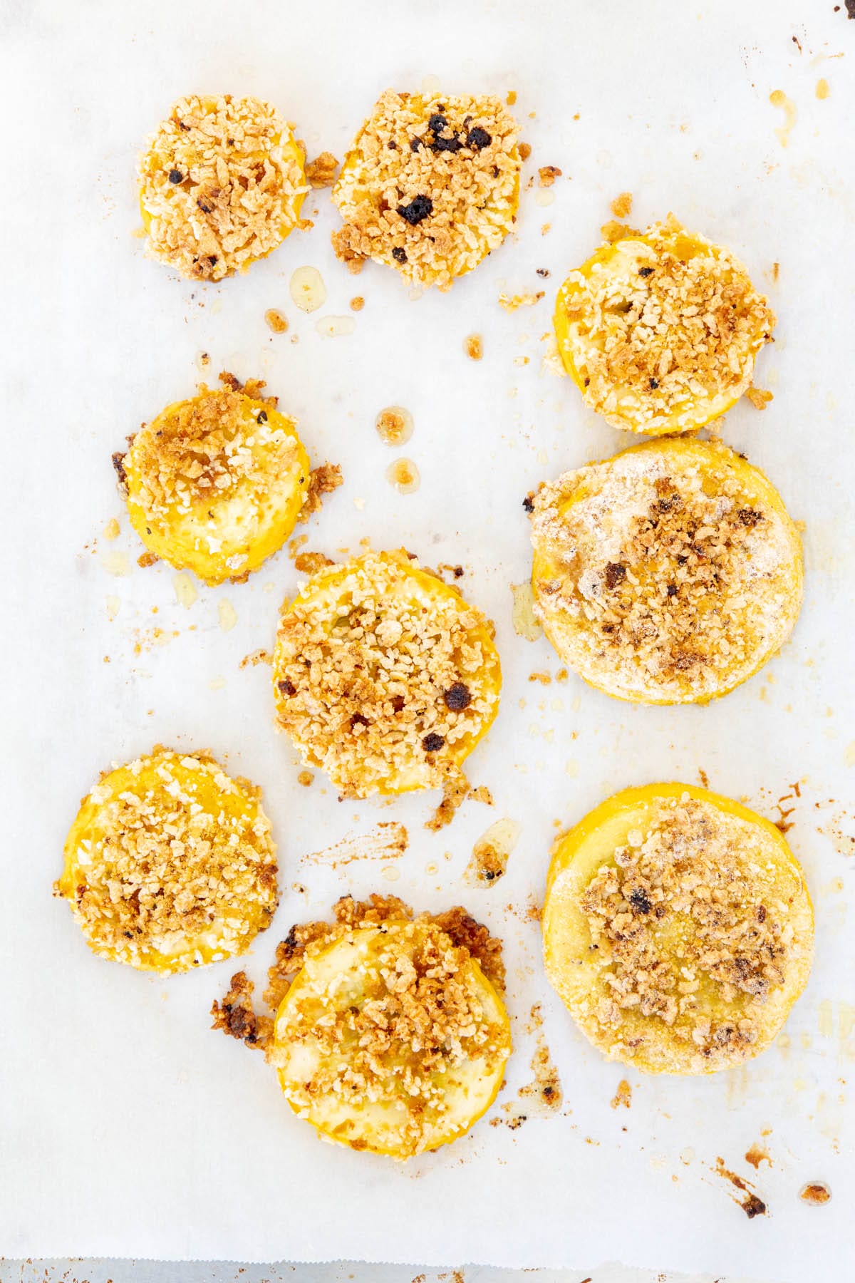 Breaded squash on a parchment paper lined baking sheet.
