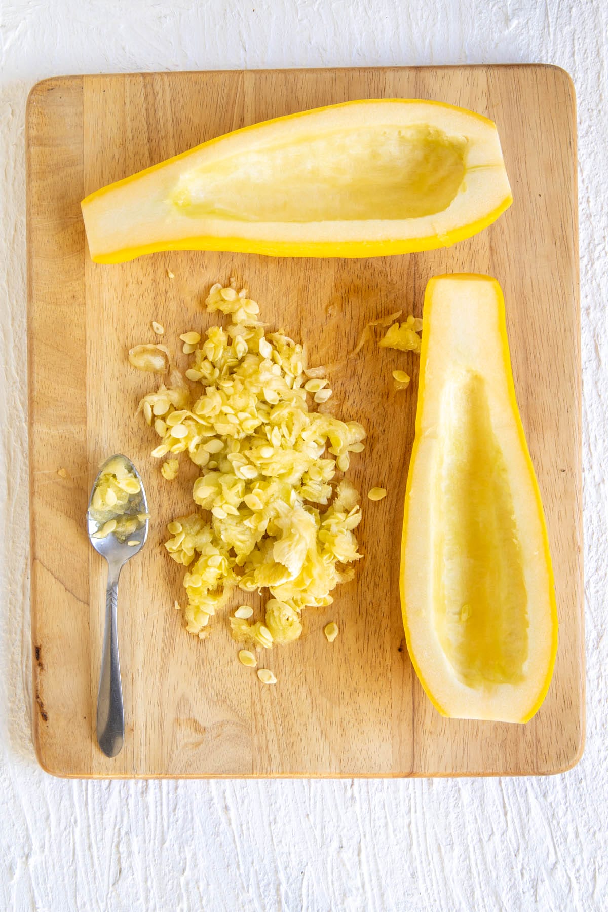 Yellow squash on a cutting board with seeds scooped out.