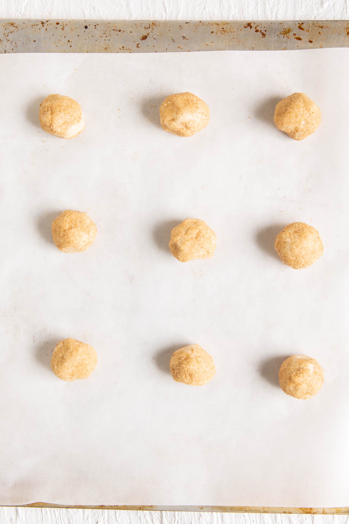 Cookie dough balls on a parchment paper lined baking sheet.