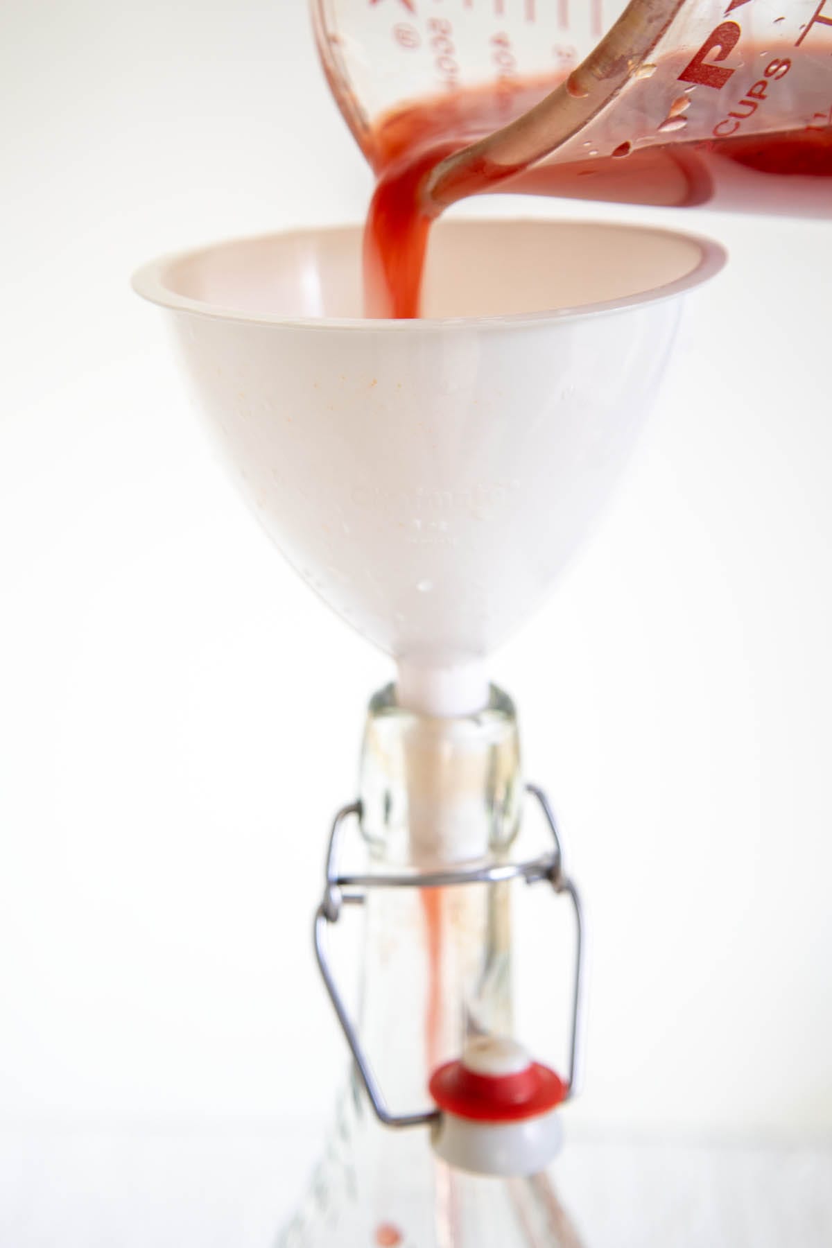 Blood orange juice being poured into a funnel into a bottle.