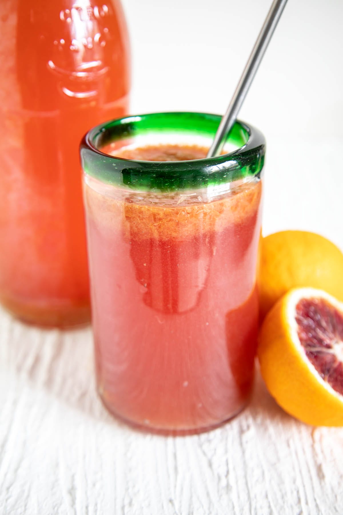 Blood Orange Kombucha in a glass and a bottle with blood oranges.