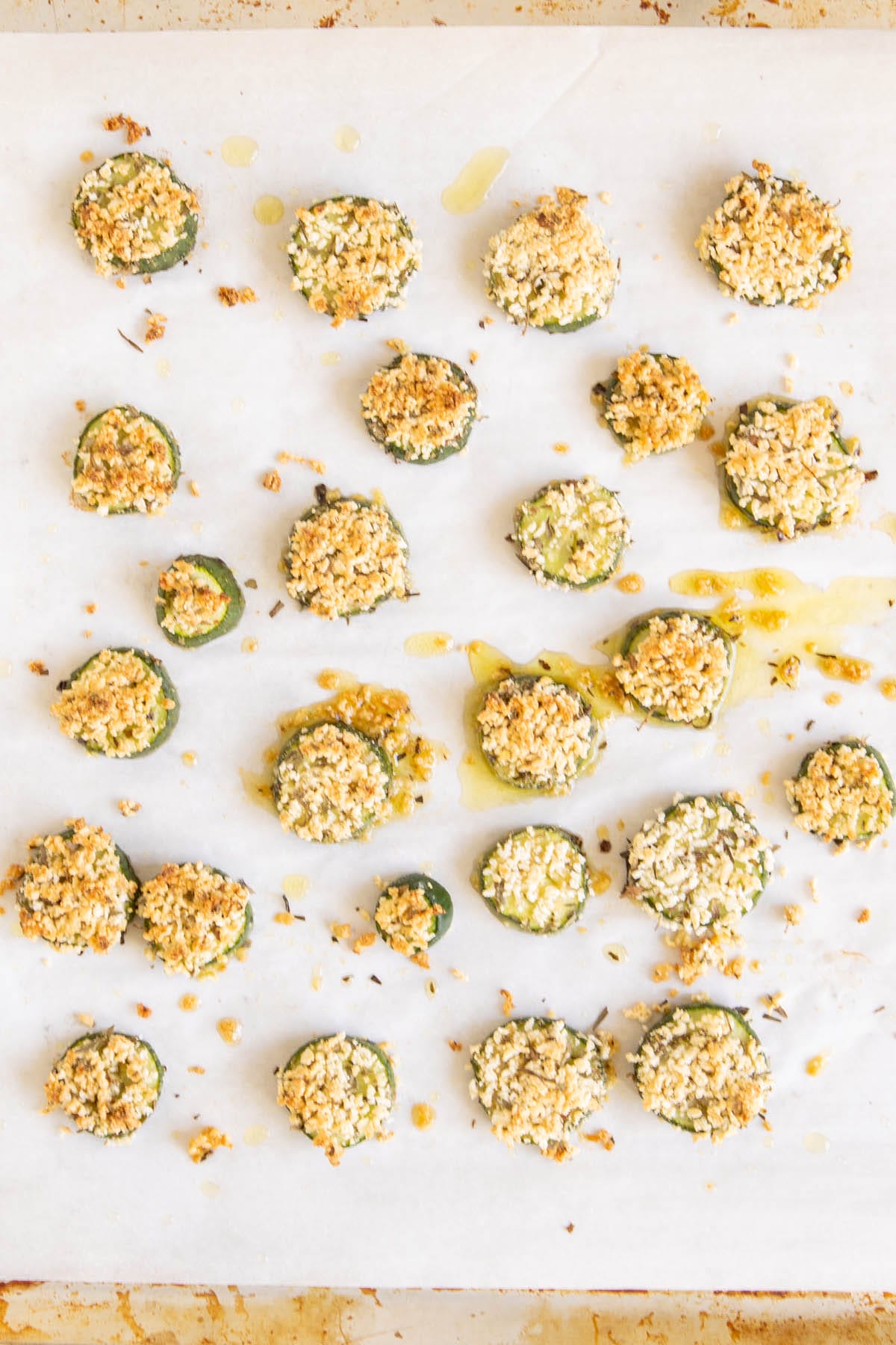 Battered and cooked cucumber on a parchment paper lined baking sheet.