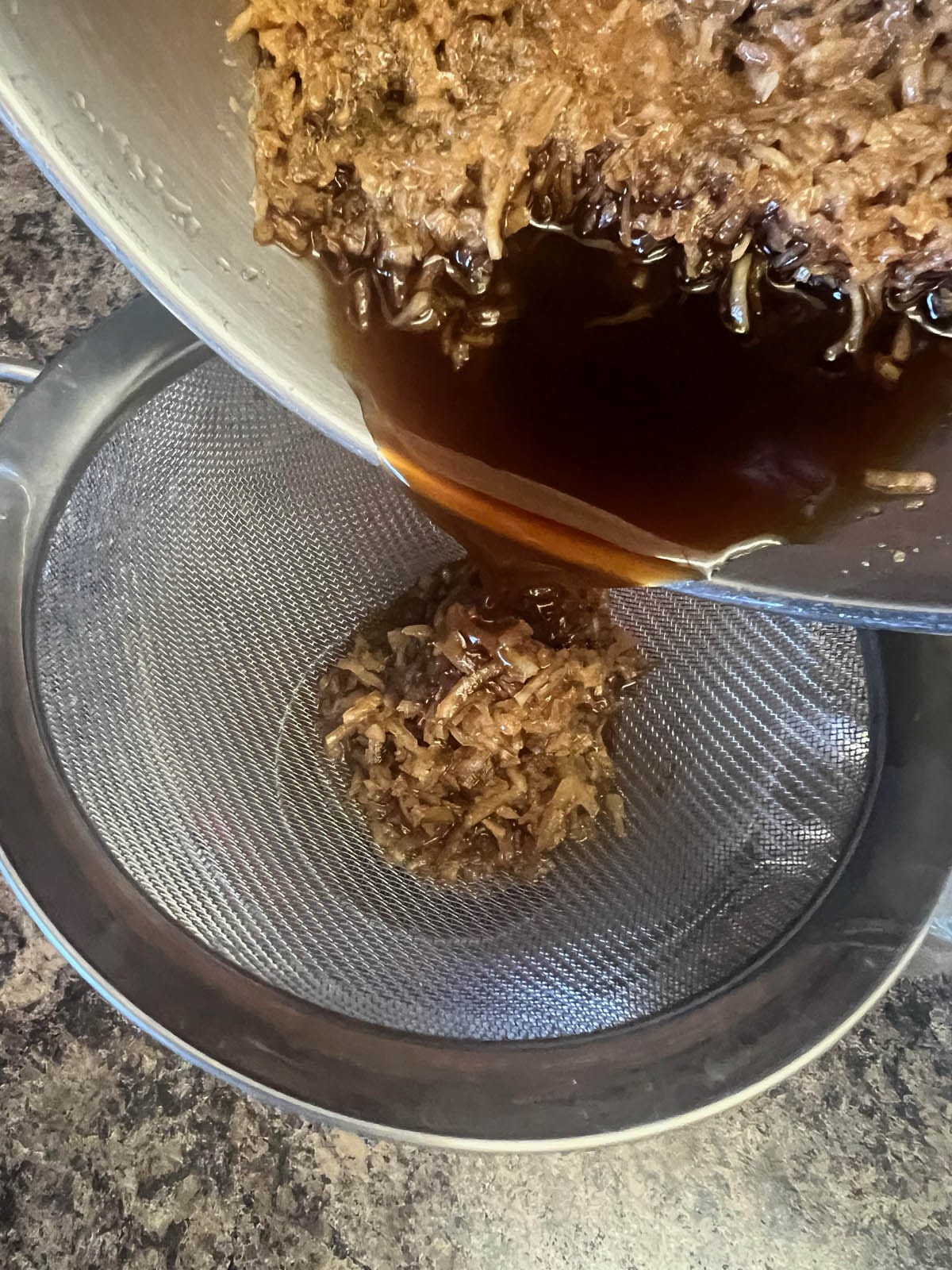 Cococnut simple syrup being poured into a pitcher with a fine mesh strainer.