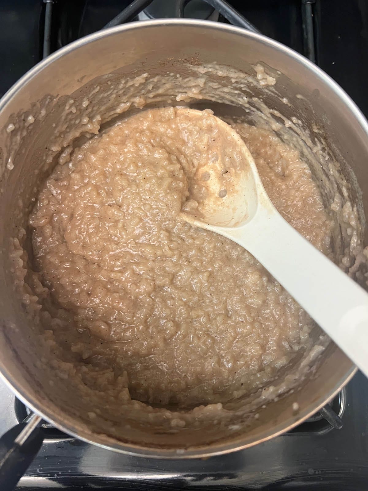Cooked rice pudding in saucepan with spoon.