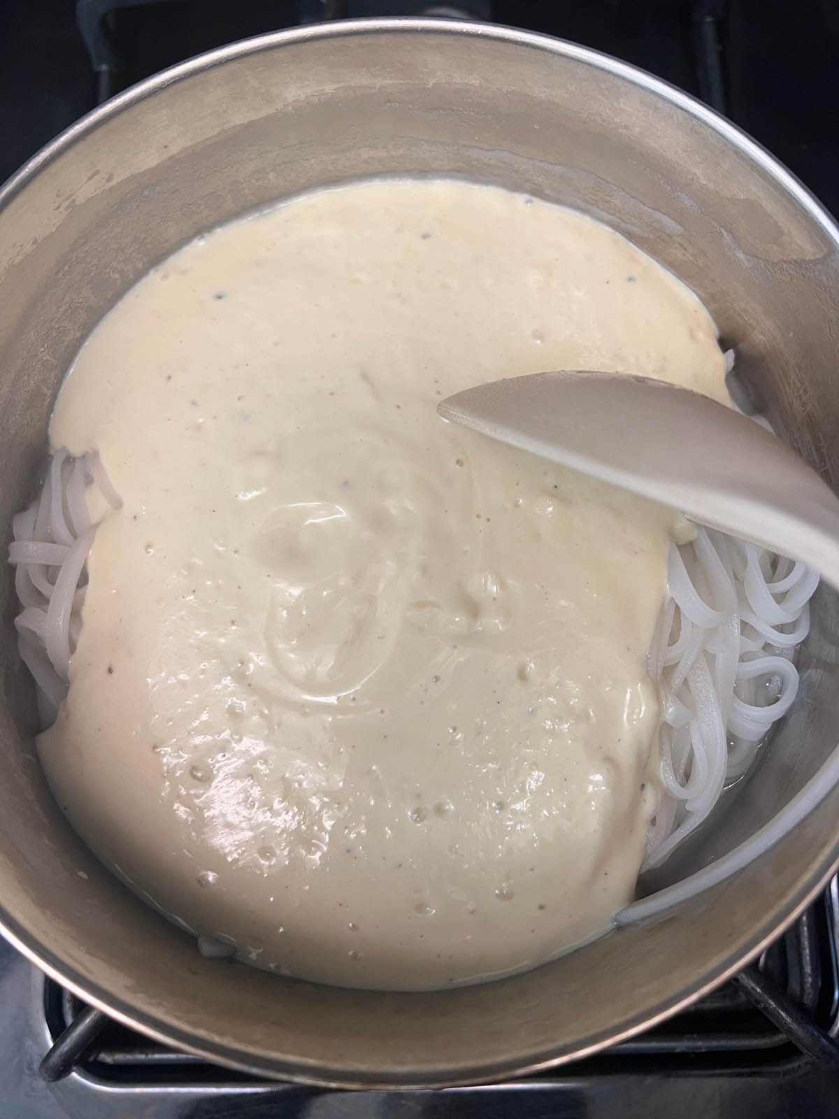 Tofu alfredo sauce added to the noodles in a saucepan.