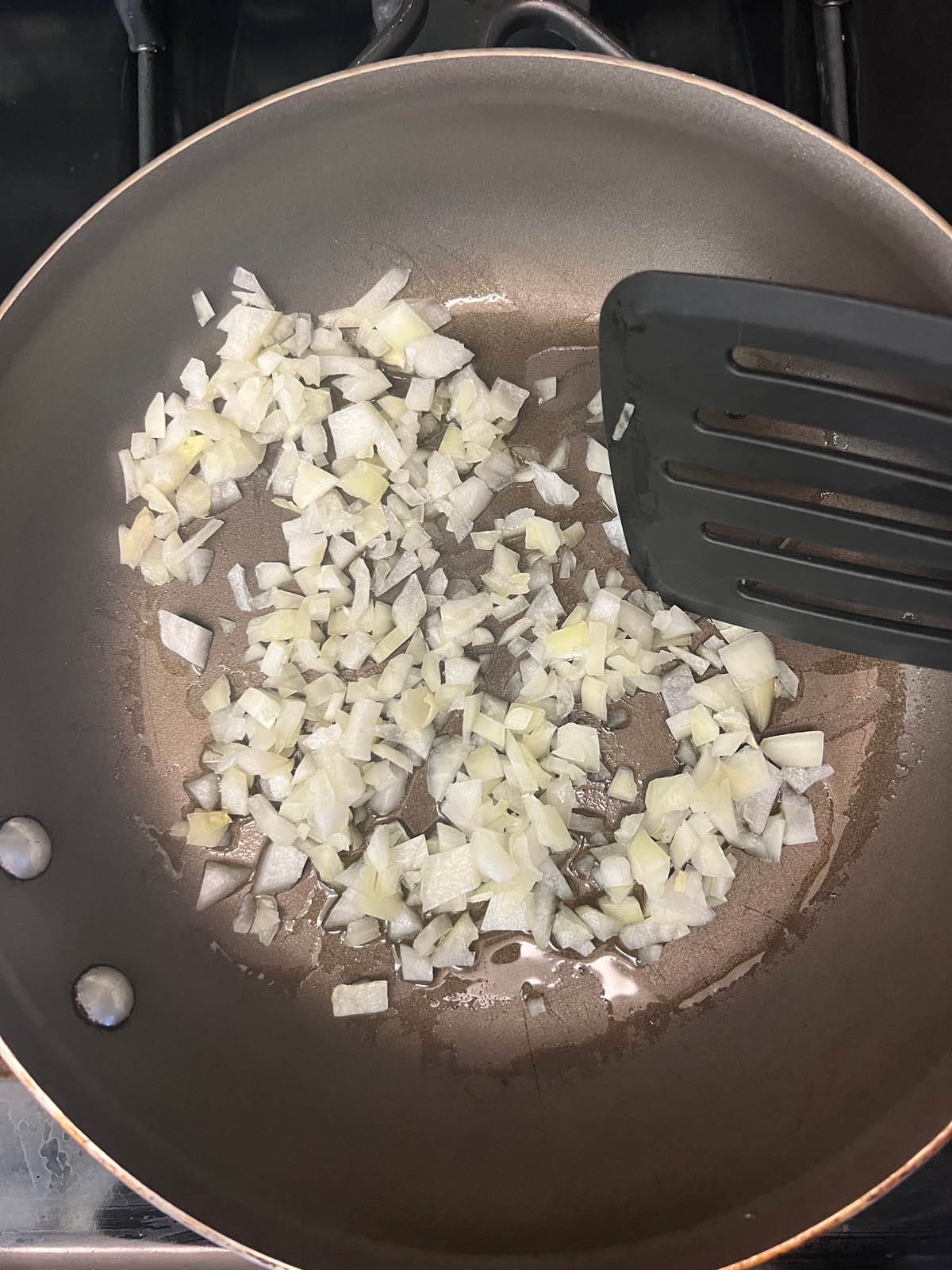 Chopped onions in a skillet with spatula.