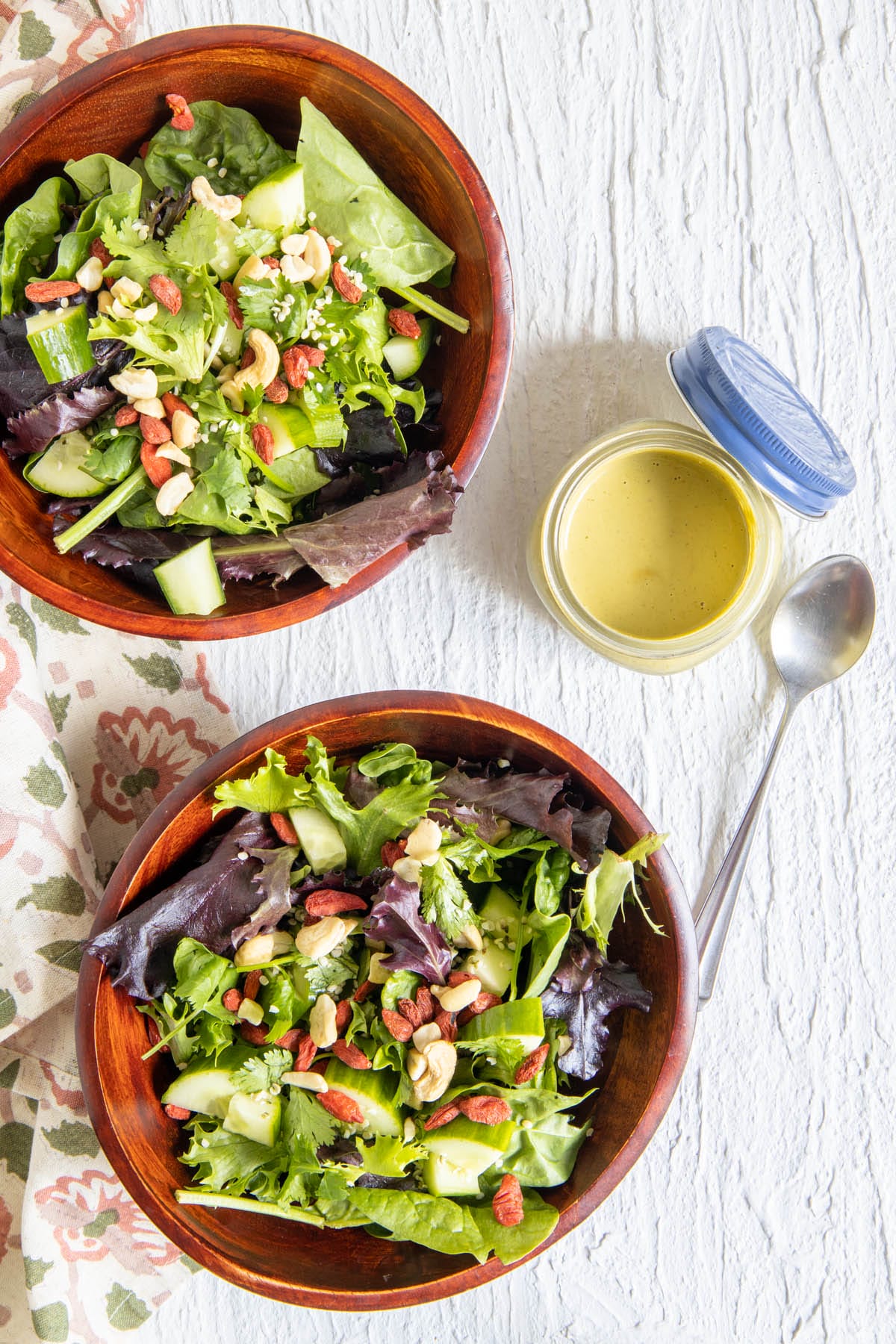 Spicy Cashew Dressing in a jar with two bowls of salad.