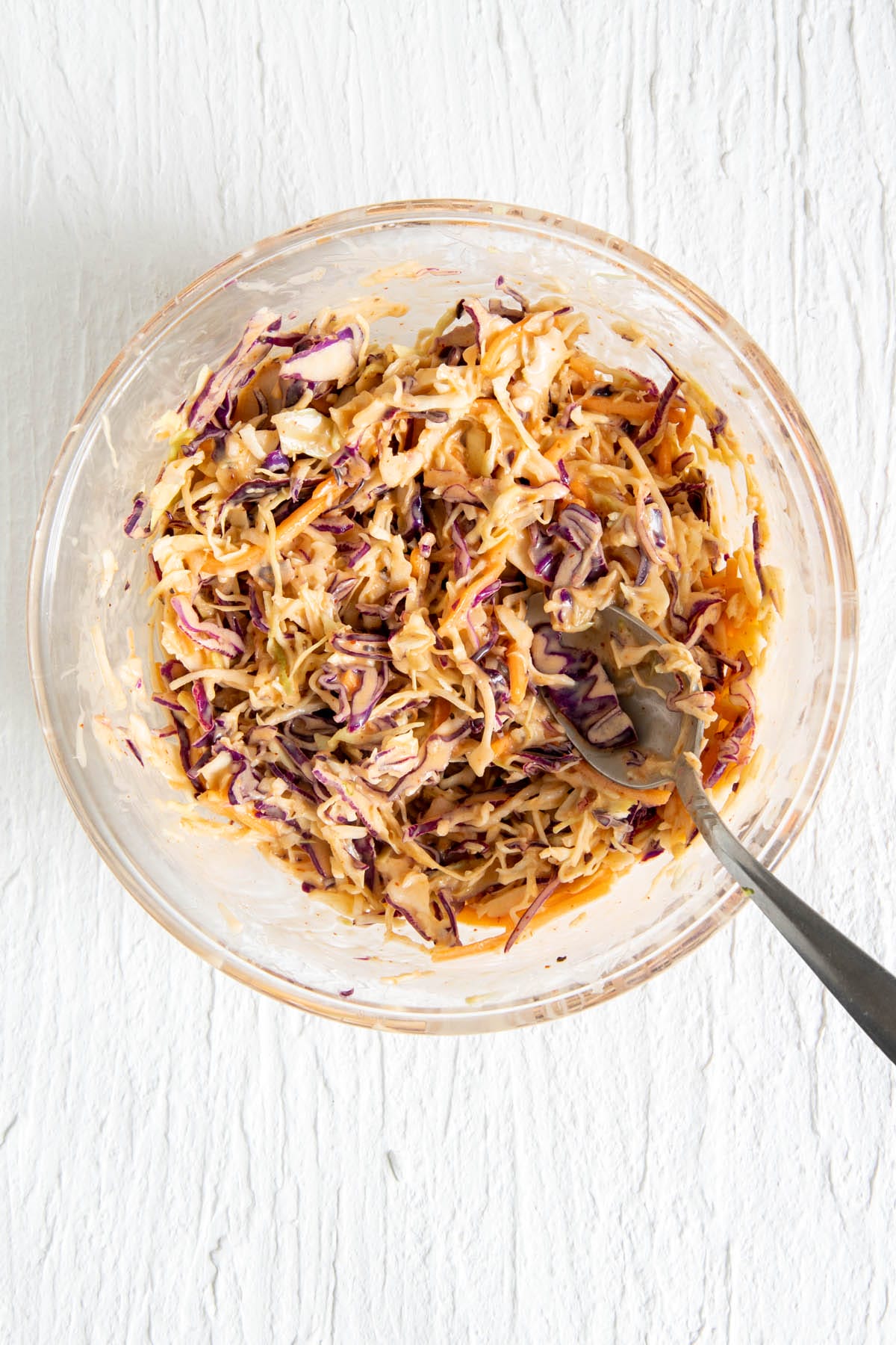 Coleslaw mix added to the sriracha coleslaw dressing in a bowl.